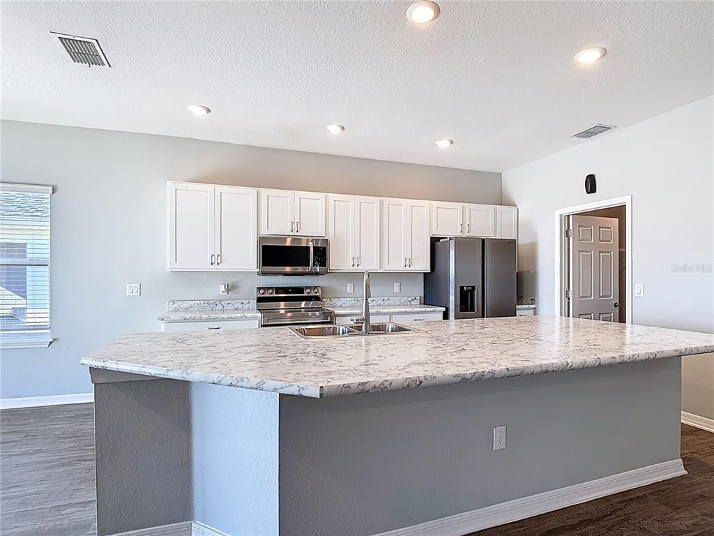 A kitchen features white cabinets, stainless steel appliances, and a large marble-patterned island countertop — 840 SYDNEY STREET, DAVENPORT, FL