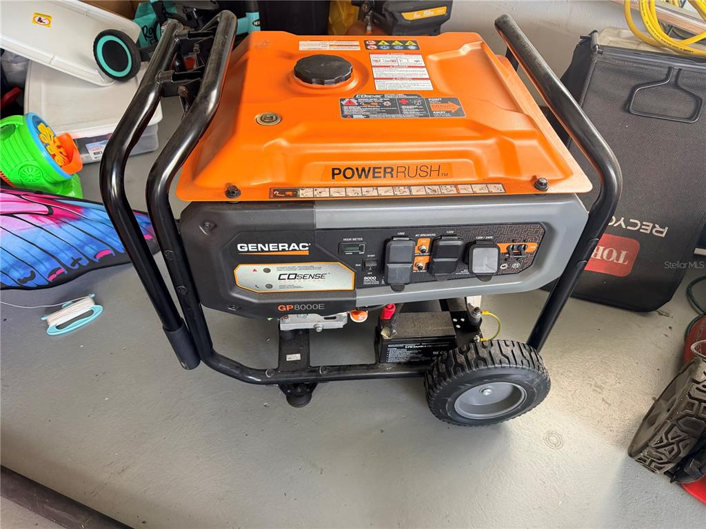 A portable Generac GP8000E generator sits on a garage floor next to various household items — 10124 HOLLY DRIVE, PORT RICHEY, FL