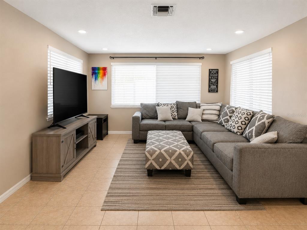A living room features a gray sectional sofa, a patterned ottoman, and a television console — 10124 HOLLY DRIVE, PORT RICHEY, FL
