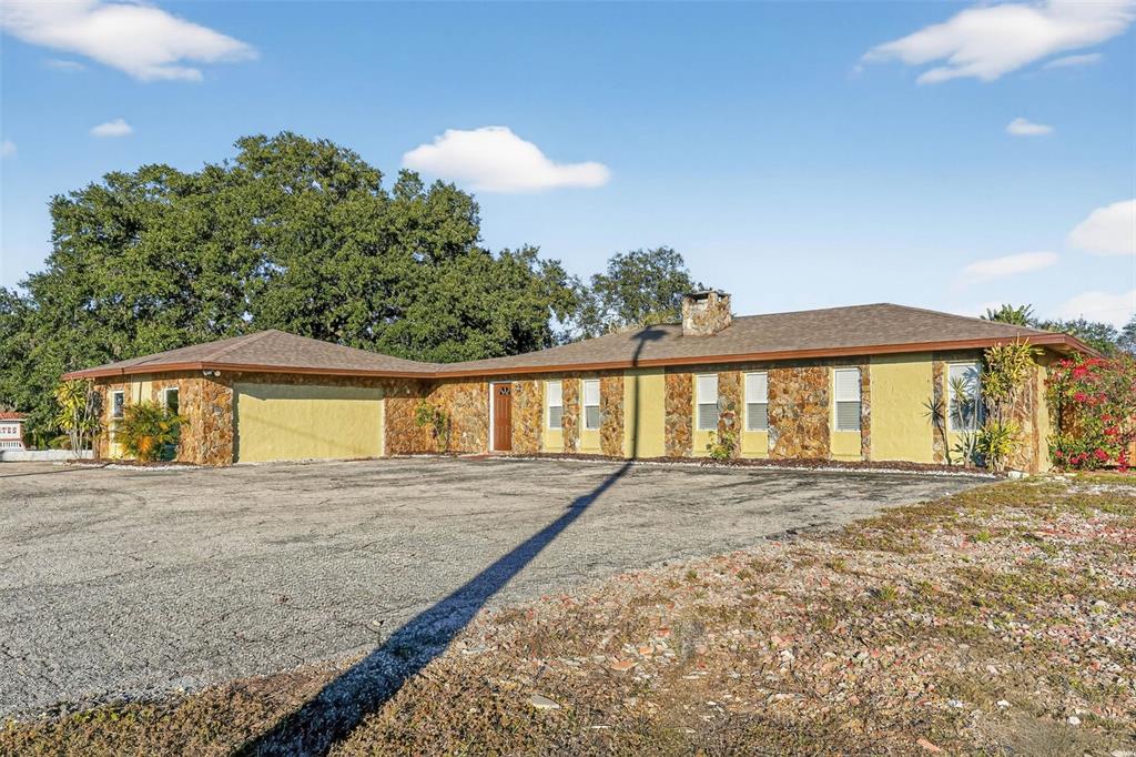A single-story house with a stone facade, a large gravel driveway, and a chimney — 8812 OAKWOOD DRIVE, LAKE WALES, FL