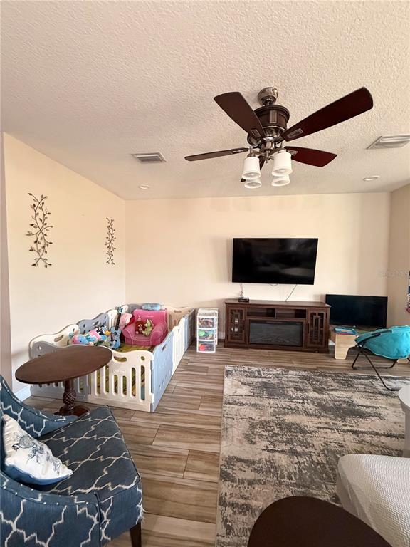 A living room features a ceiling fan, a television on a console, and a playpen — 308 CORBETT BLUFF DRIVE, RUSKIN, FL