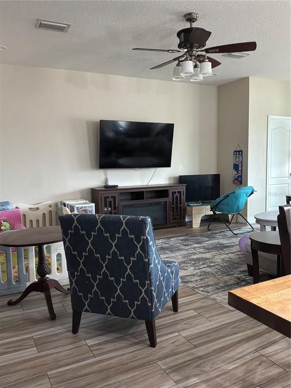 A living room features a wall-mounted television, a ceiling fan, and wood-look tile flooring — 308 CORBETT BLUFF DRIVE, RUSKIN, FL