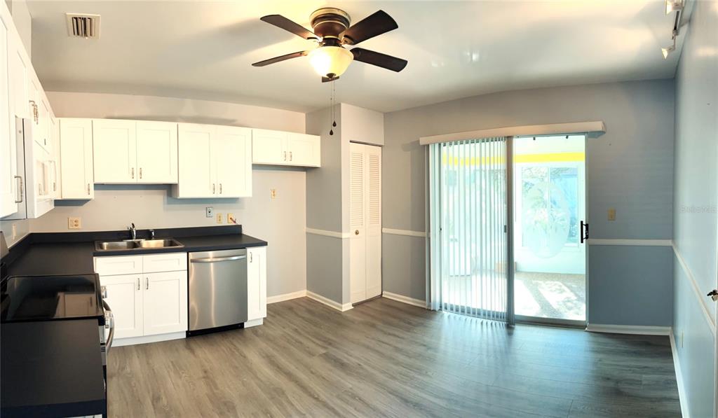 A kitchen with white cabinets, stainless steel dishwasher, and wood-look flooring next to sliding doors — 26 FORE DRIVE, NEW SMYRNA BEACH, FL