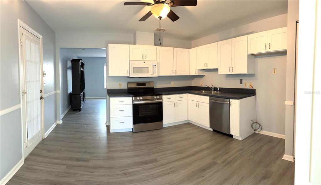 A kitchen with white cabinets, stainless steel appliances, and gray wood-look flooring — 26 FORE DRIVE, NEW SMYRNA BEACH, FL