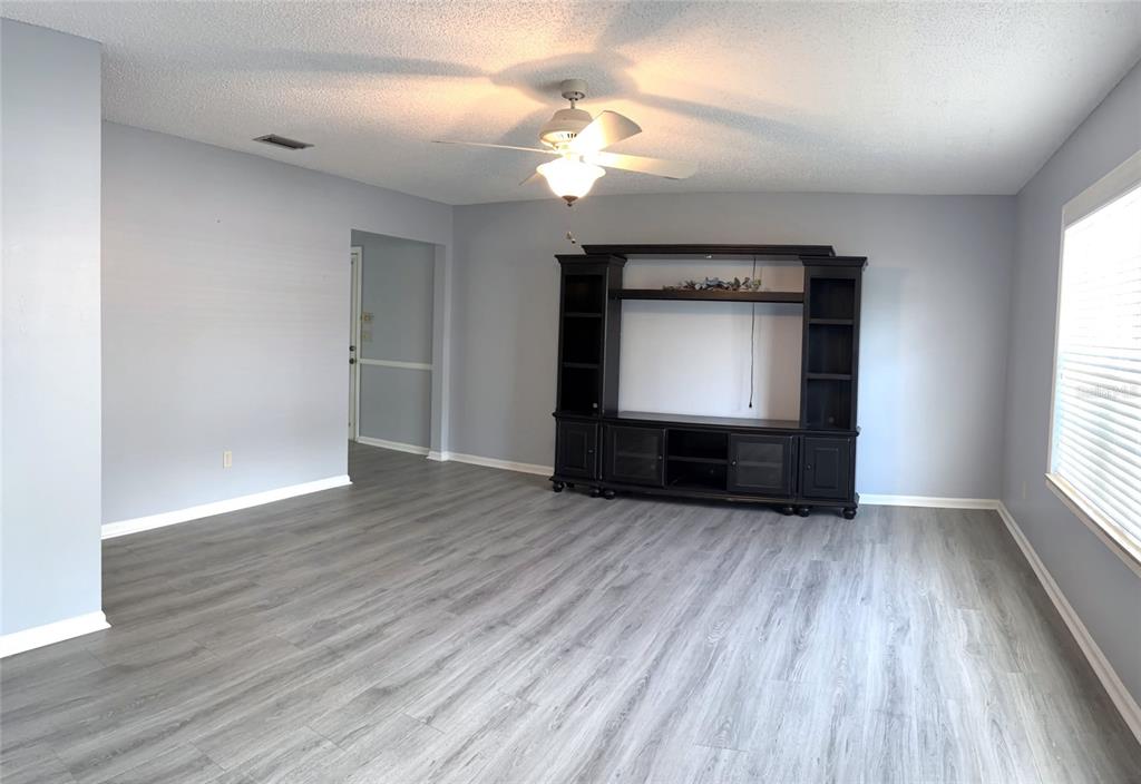 A living room features light gray walls, wood-look flooring, a ceiling fan, and a media console — 26 FORE DRIVE, NEW SMYRNA BEACH, FL