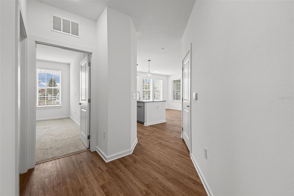 A hallway with wood-look flooring leads to a kitchen and a carpeted room — 1700 RANCH ROAD UNIT B2-6107, NOKOMIS, FL