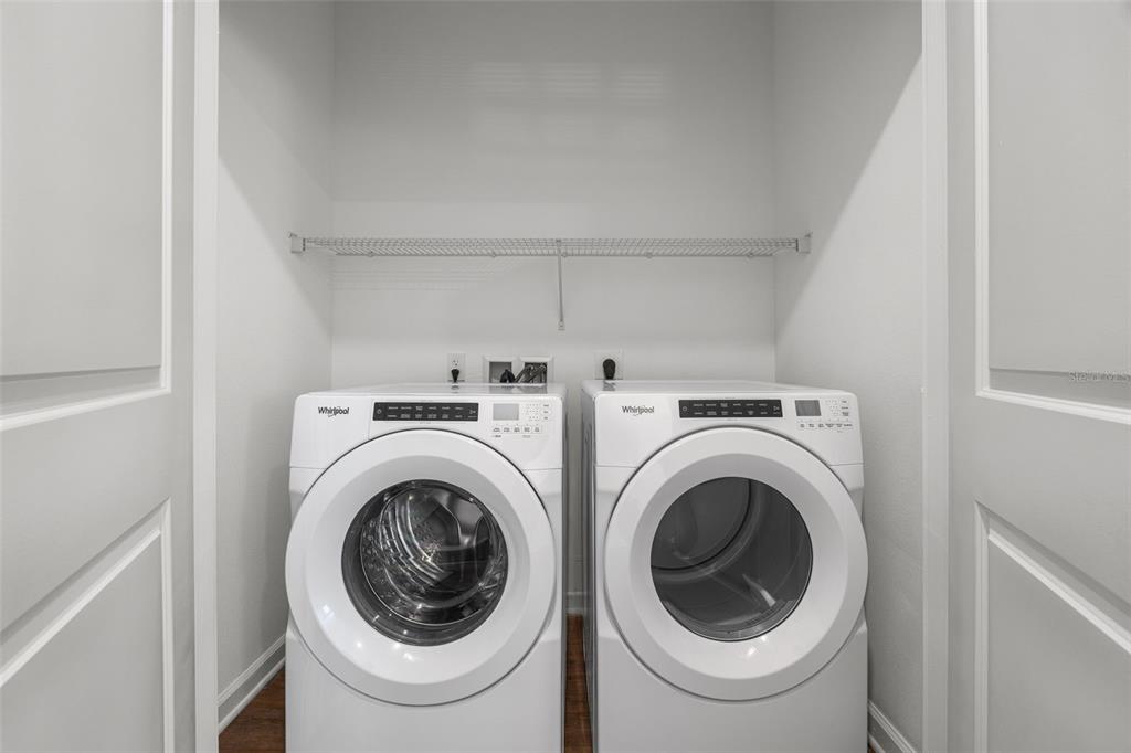 A laundry closet contains a white Whirlpool washer and dryer beneath a wire shelf — 1700 RANCH ROAD UNIT B2-6107, NOKOMIS, FL