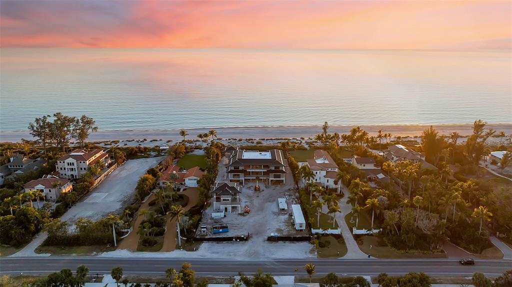 An aerial view shows a beachfront construction site between two finished houses at sunset — 5965 GULF OF MEXICO DRIVE, LONGBOAT KEY, FL