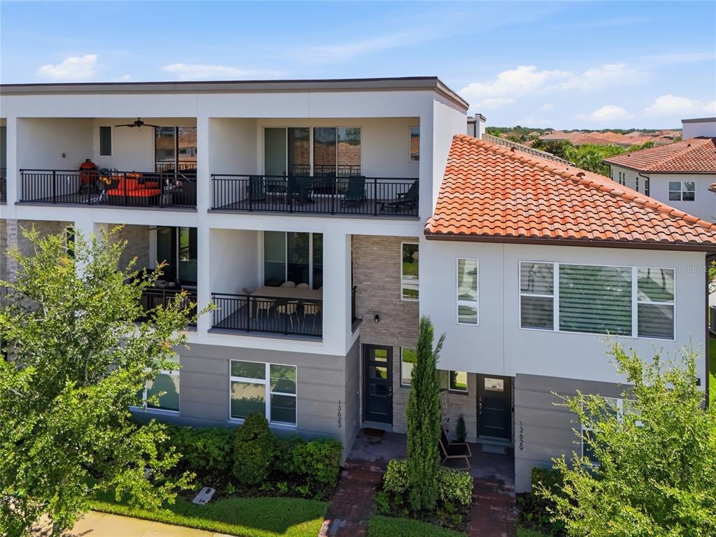An exterior view of a multi-story residential building with balconies, a tiled roof, and landscaping — 13623 LARKTON LANE, ORLANDO, FL