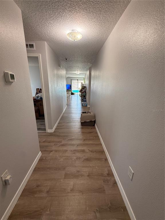 A hallway with light-colored walls and wood-look flooring leads toward a living area — 2185 ROCK DRIVE, POINCIANA, FL