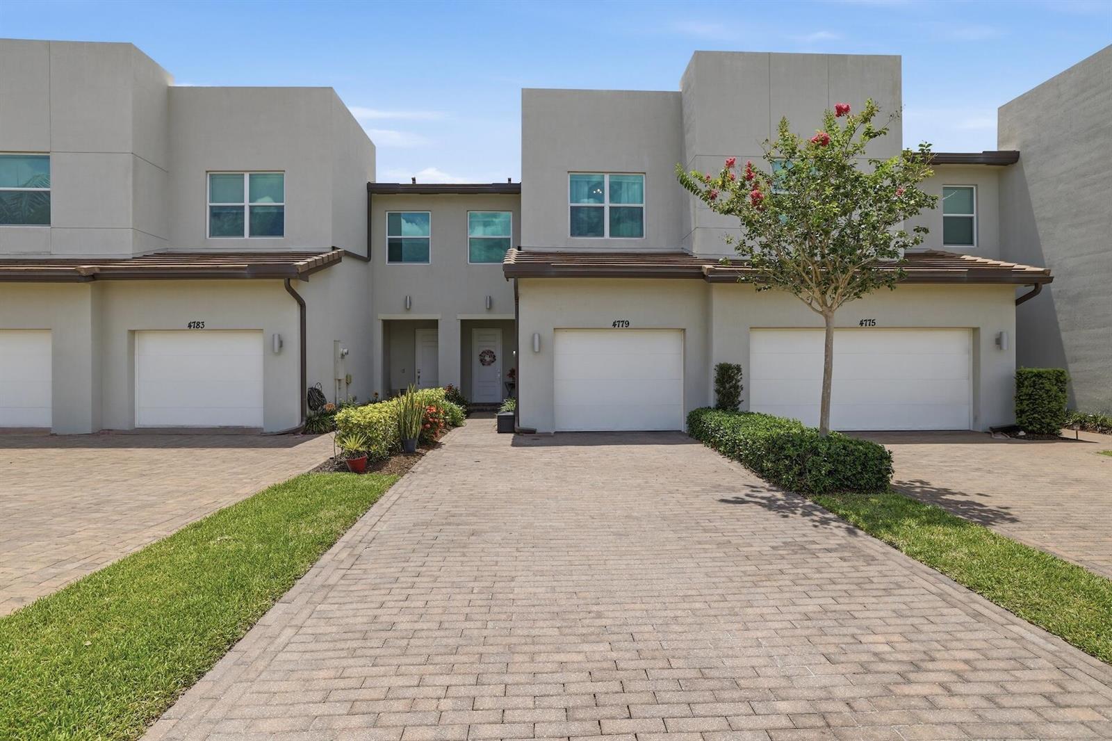 A row of three modern townhouses features beige stucco exteriors, white garage doors, and brick driveways — 4779 Navali Drive, Lake Worth FL 33467, LAKE WORTH, FL