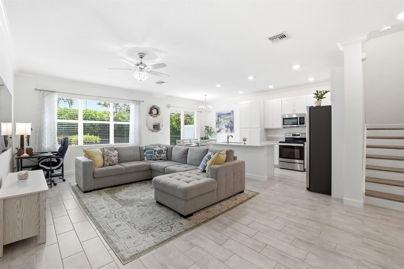 A bright open-concept living room and kitchen featuring light tile flooring and a gray sectional — 4779 Navali Drive, Lake Worth FL 33467, LAKE WORTH, FL