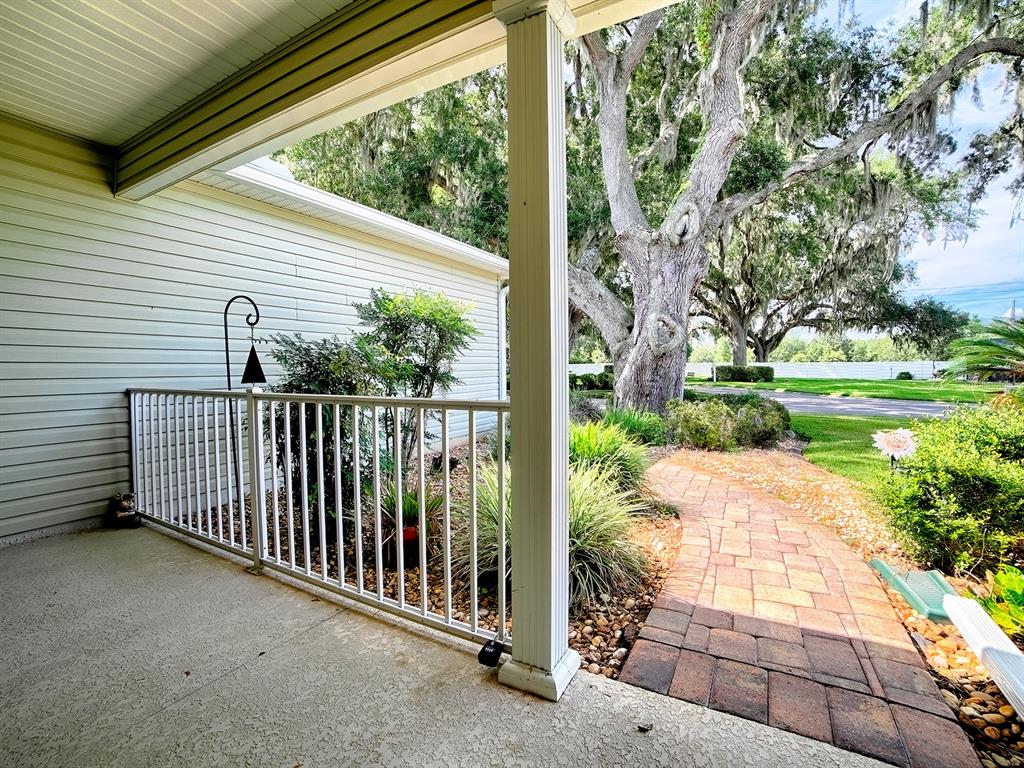 A covered patio features a white railing, a brick walkway, and large oak trees nearby — 1033 MEADOWBEND DRIVE, LEESBURG, FL