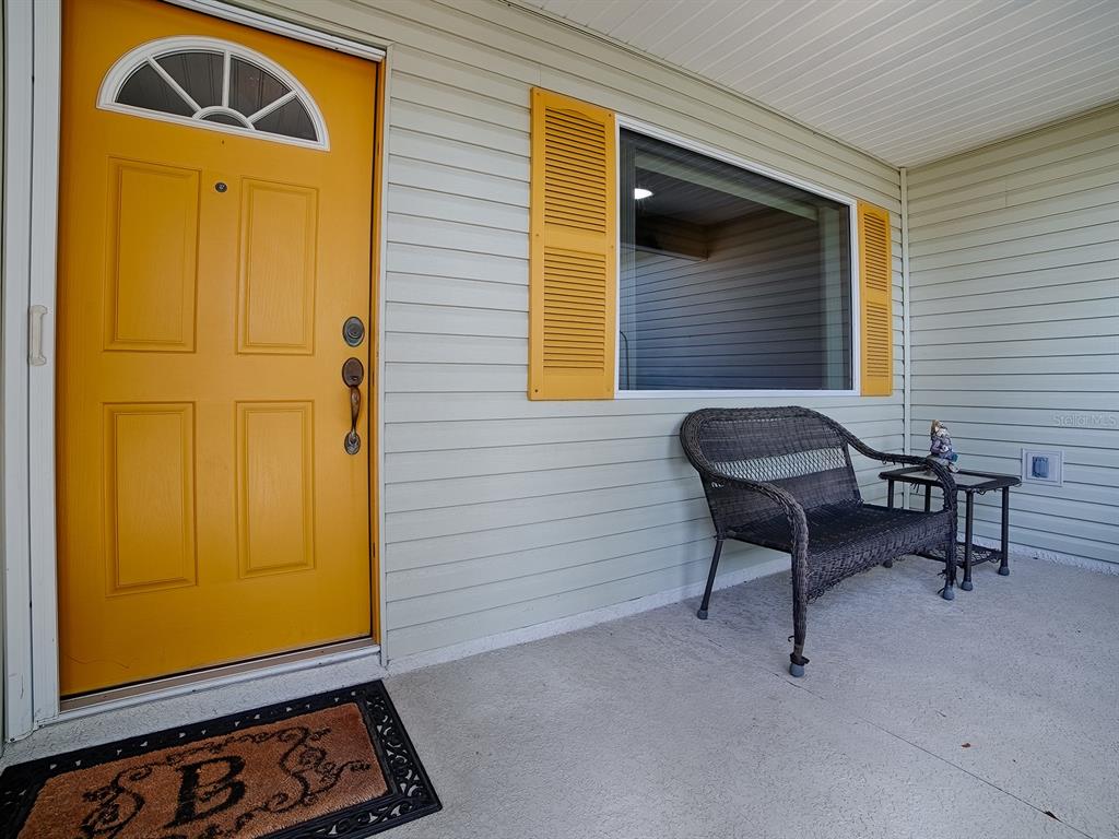 A front porch features a yellow door, a window with yellow shutters, and a bench — 1033 MEADOWBEND DRIVE, LEESBURG, FL