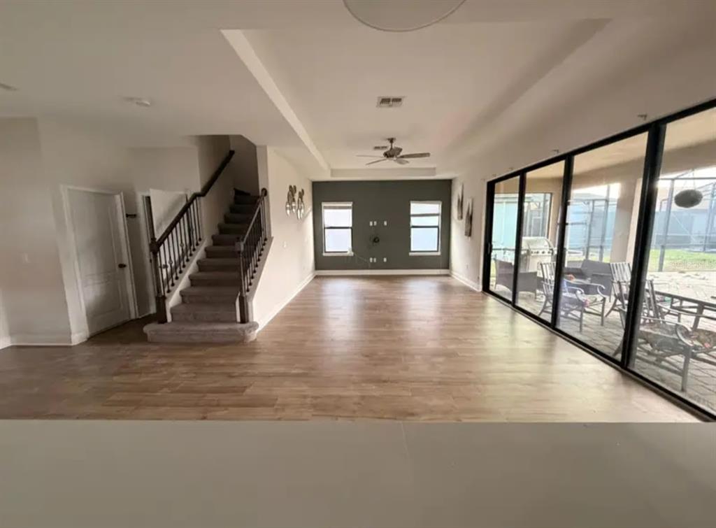 An open living area features wood-look flooring, a staircase with dark railings, and large sliding doors — 187 BROOKES PLACE, HAINES CITY, FL
