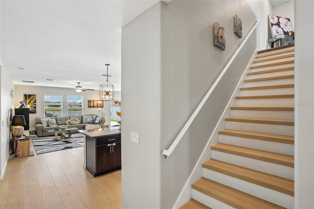 A staircase with light wood treads leads upward beside an open-concept living and kitchen area — 15608 MILLER CREEK DRIVE, SUN CITY CENTER, FL