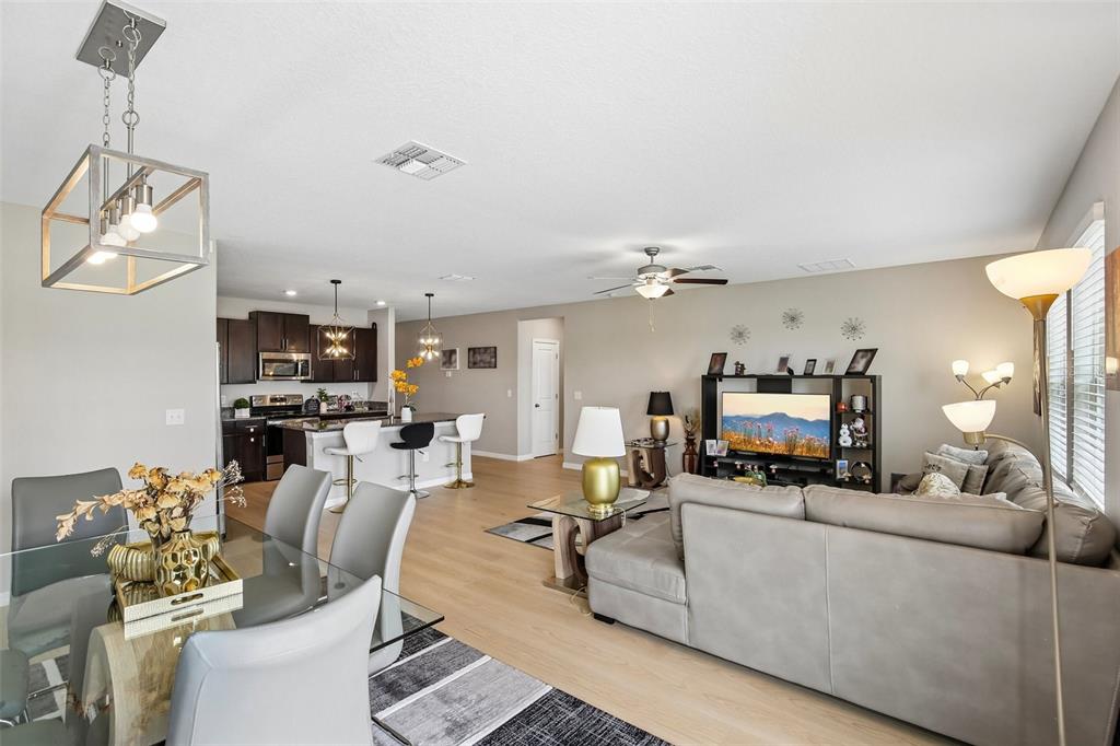 An open-concept living and dining area features light wood flooring, a kitchen island, and furniture — 15608 MILLER CREEK DRIVE, SUN CITY CENTER, FL