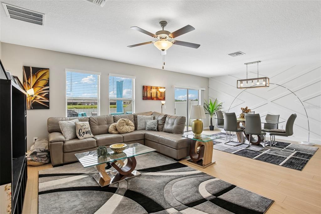 A living and dining area features a sectional sofa, glass tables, and a geometric wall — 15608 MILLER CREEK DRIVE, SUN CITY CENTER, FL