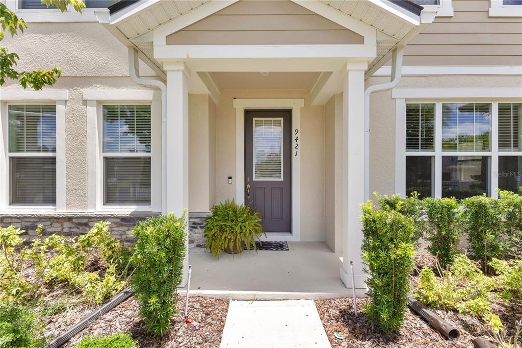 The front entrance of a house features a covered porch, a gray door, and landscaping — 9421 RANDAL PARK BOULEVARD, ORLANDO, FL