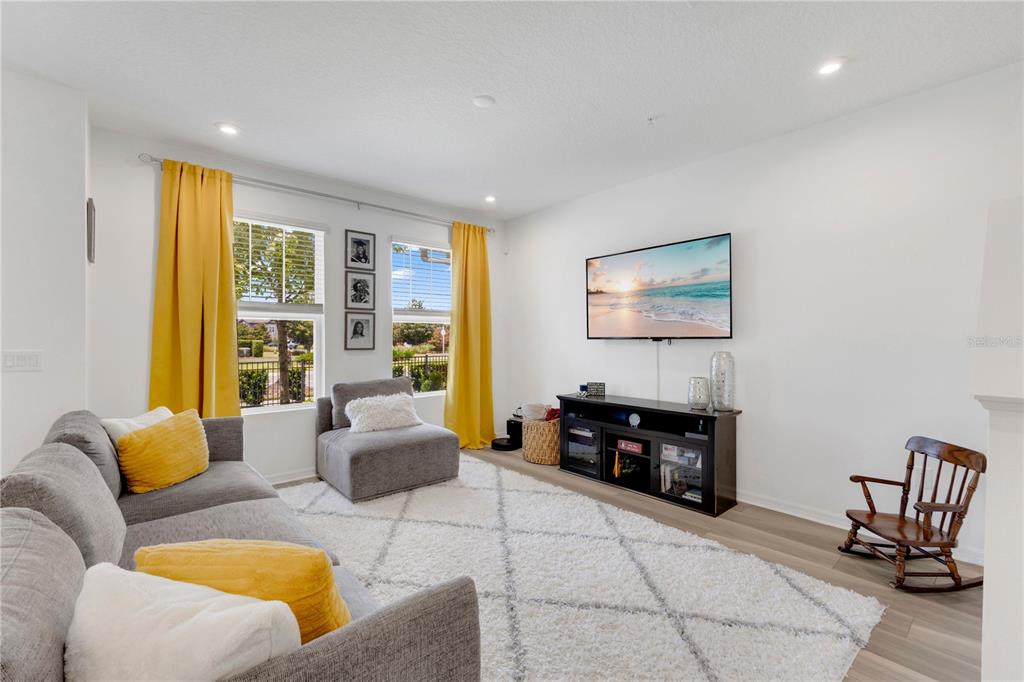 An open-concept living and dining area features light wood flooring, a gray sofa, and furniture — 9421 RANDAL PARK BOULEVARD, ORLANDO, FL