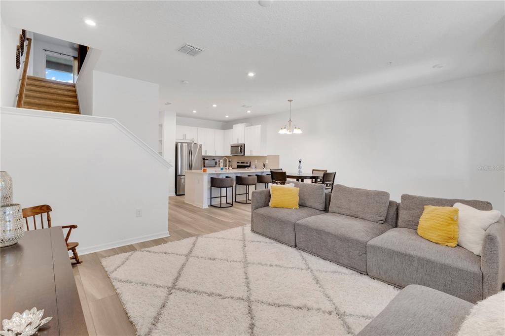 An open-concept living room features a gray sectional sofa, a white rug, and a kitchen — 9421 RANDAL PARK BOULEVARD, ORLANDO, FL