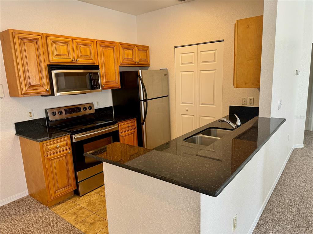 A kitchen with wood cabinets, black countertops, stainless steel appliances, and a breakfast bar — 832 GRAND REGENCY POINT UNIT 204, ALTAMONTE SPRINGS, FL