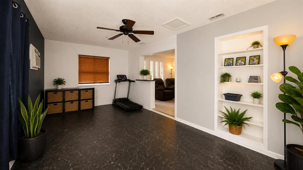 A room with dark flooring, a treadmill, a built-in bookshelf, and a ceiling fan — 3319 AVENUE U NW, WINTER HAVEN, FL