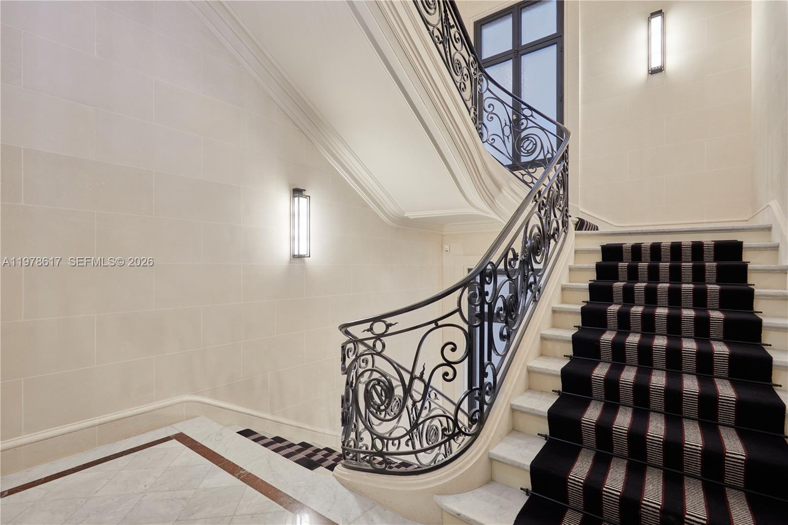 A curved staircase with an ornate iron railing features a black and white striped runner — 11 RUE ST DOMINIQUE, FR, FR