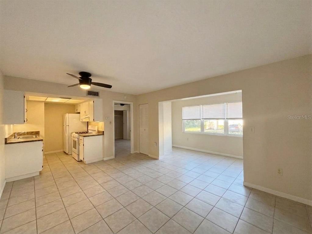 A kitchen with white cabinets and tile flooring opens into a living area with windows — 1103 CYPRESS GARDENS BOULEVARD UNIT 30, WINTER HAVEN, FL
