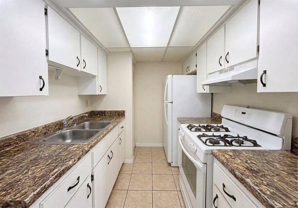 A galley kitchen features white cabinets, brown granite-look countertops, a white stove, and tile flooring — 1103 CYPRESS GARDENS BOULEVARD UNIT 30, WINTER HAVEN, FL