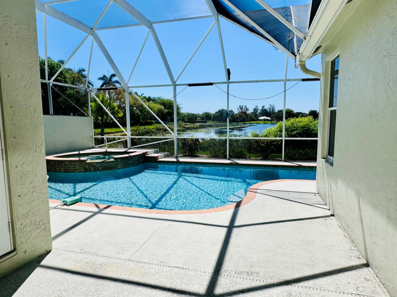 A screened-in patio features a swimming pool, a raised spa, and a view of a lake — 9360 Cove Point Circle, Boynton Beach FL 33472, BOYNTON BEACH, FL