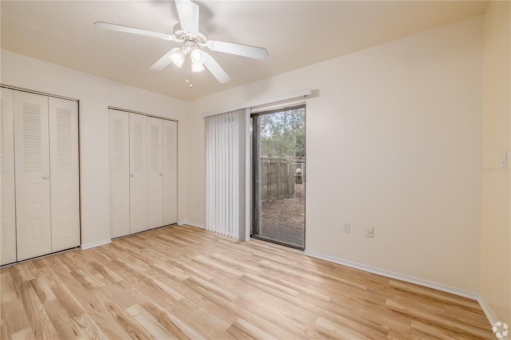 An empty bedroom features light wood-look flooring, two sets of closet doors, and a sliding door — 422 SW 69TH STREET, GAINESVILLE, FL