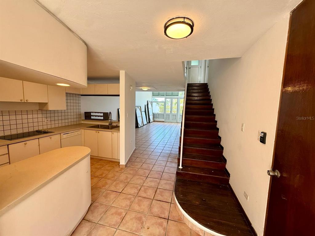 A kitchen with light cabinets and tile floors leads to a staircase and living area — #124 VILLAS DE GOLF OESTE, DORADO, PR