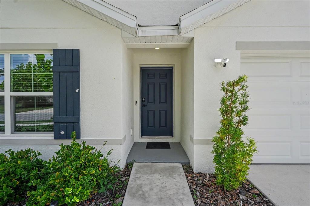 The exterior of a home features a dark blue front door, shutters, and landscaping — 5038 CADIZ COURT, BROOKSVILLE, FL