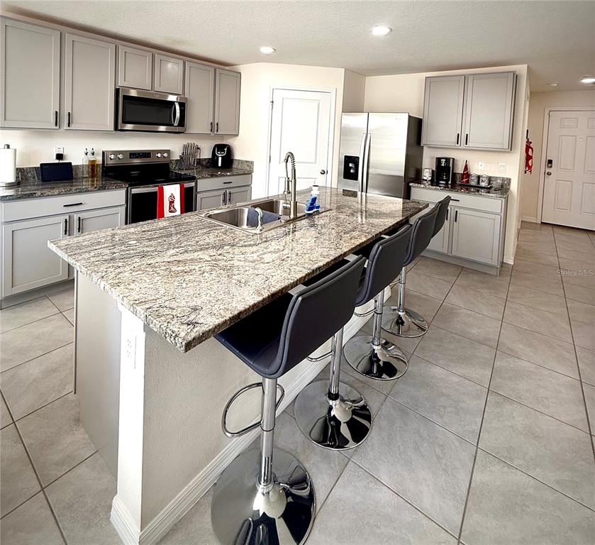 A kitchen features gray cabinets, granite countertops, a central island with bar stools, and appliances — 3727 CAPRI COAST DRIVE, PLANT CITY, FL