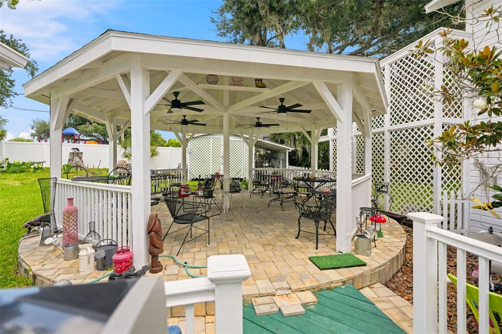 A white gazebo with a paver floor and ceiling fans sits in a grassy backyard — 65 OLIVE STREET, BROOKSVILLE, FL