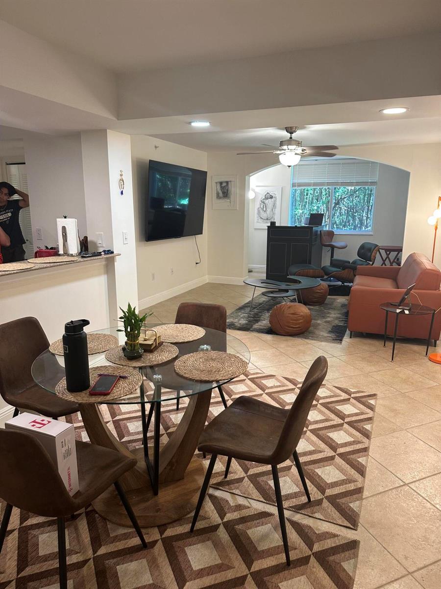 An open-concept living and dining area features tile flooring, a glass table, and a television — 400 Scotia Drive # 103, Hypoluxo FL 33462, HYPOLUXO, FL
