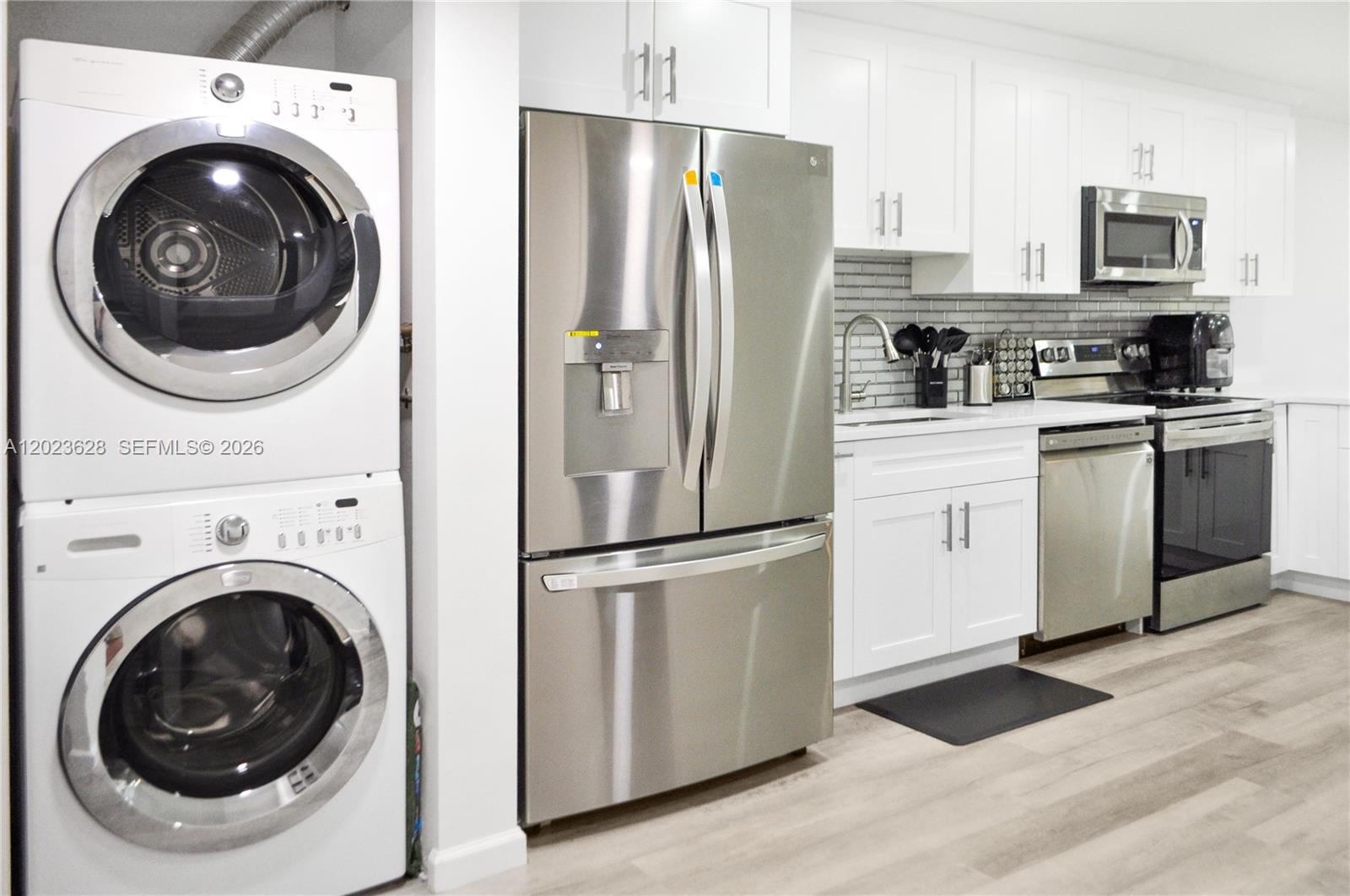 A kitchen features white cabinets, stainless steel appliances, and a stacked washer and dryer unit — 1021 Mockingbird Ln # 202, Plantation FL 33324, PLANTATION, FL