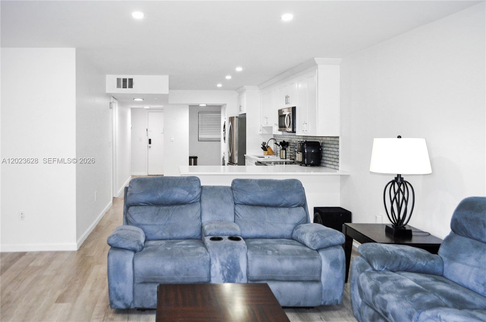 A living room with blue reclining sofas faces an open kitchen with white cabinetry — 1021 Mockingbird Ln # 202, Plantation FL 33324, PLANTATION, FL