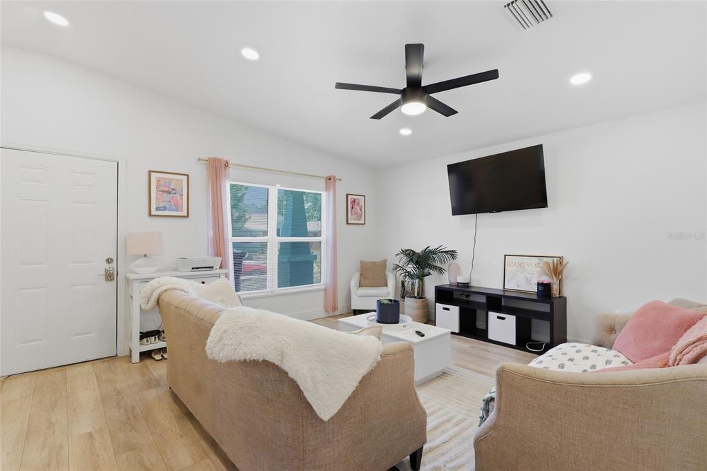 A living room features light wood flooring, a ceiling fan, and a wall-mounted television — 1918 W PINE STREET, TAMPA, FL