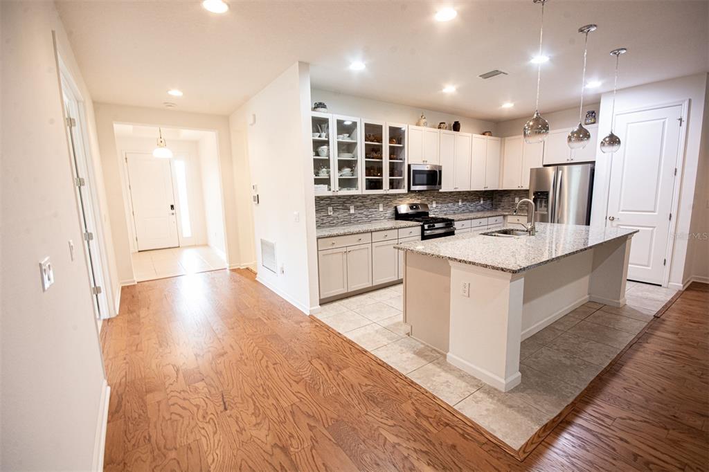 An open-concept living room and kitchen featuring wood flooring, neutral furniture, and a dining area — 215 AVENHAM DRIVE, DELAND, FL