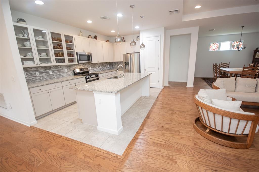 A kitchen with white cabinets, granite countertops, and an island sits beside a hardwood-floored entryway — 215 AVENHAM DRIVE, DELAND, FL