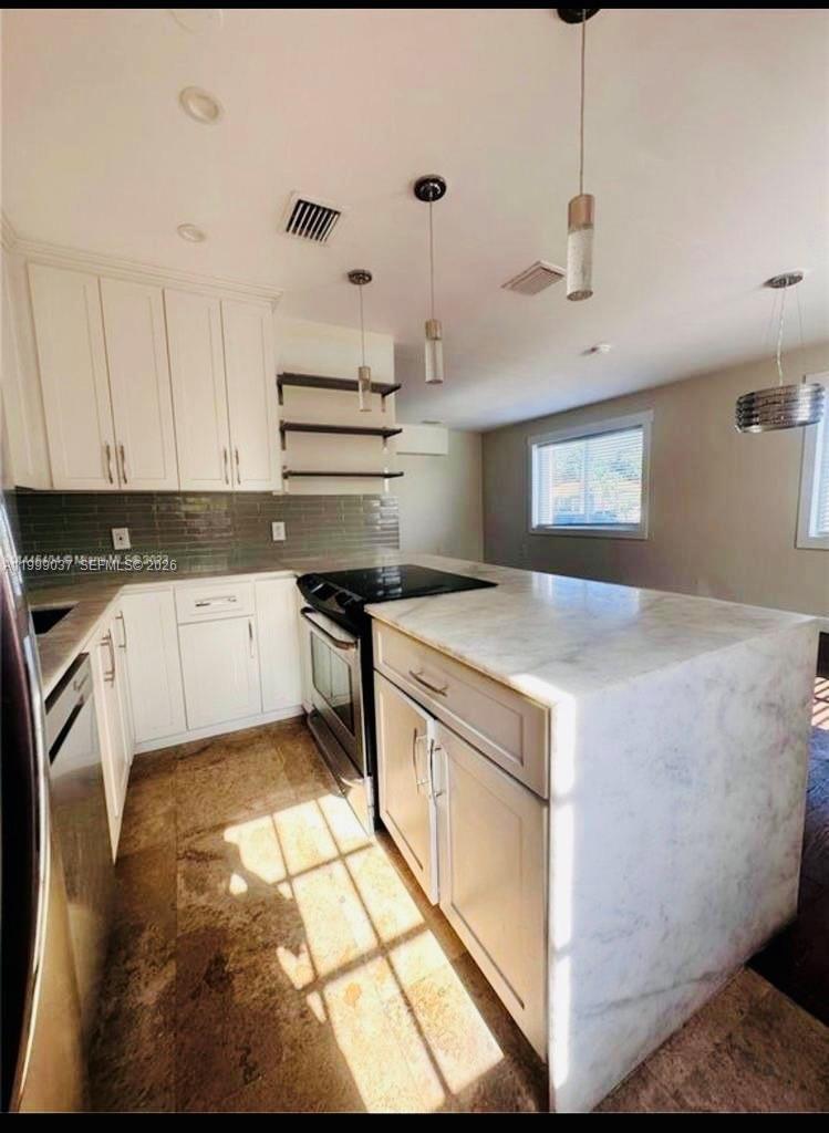 A kitchen features white cabinetry, a marble-topped island, and a glass-tiled backsplash — 2775 SW 1st St, Miami FL 33135, MIAMI, FL