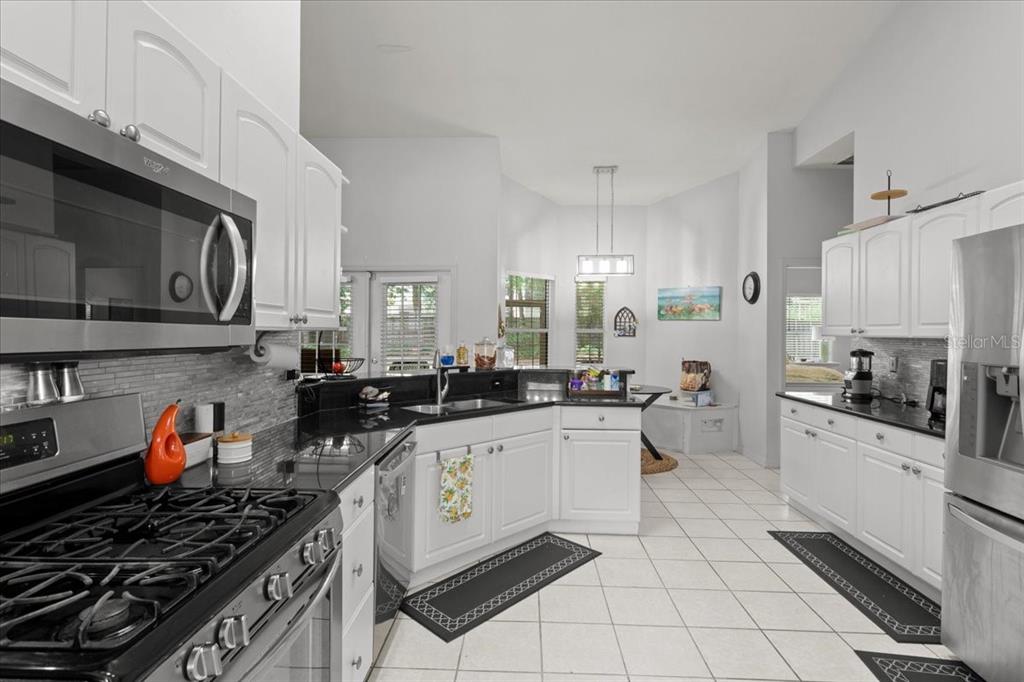 A kitchen with white cabinets, black countertops, stainless steel appliances, and light tile flooring — 5514 NW 78TH LANE, GAINESVILLE, FL