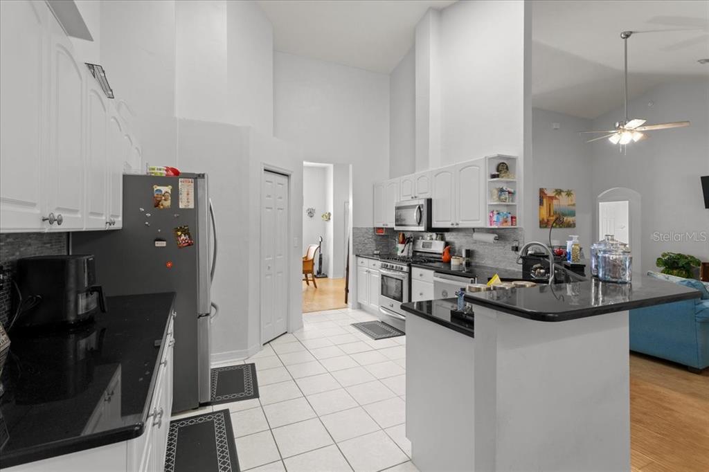 A kitchen with white cabinets, black countertops, and tile flooring opens to a living area — 5514 NW 78TH LANE, GAINESVILLE, FL