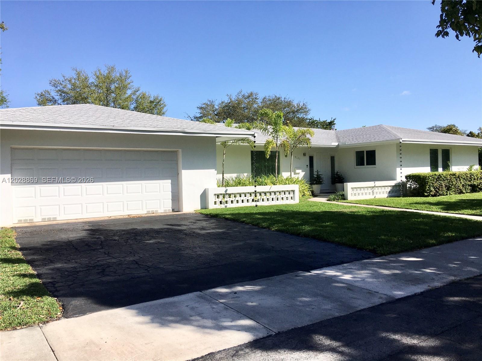 A single-story white house features a two-car garage, a paved driveway, and decorative concrete walls — 9121 SW 85th St, Miami FL 33173, MIAMI, FL