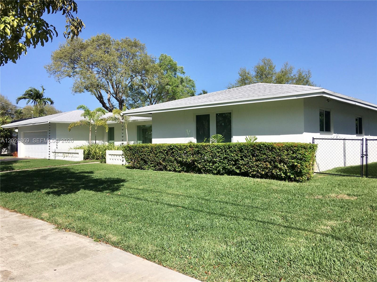 A white single-story house features a green hedge, a chain-link fence, and a grassy lawn — 9121 SW 85th St, Miami FL 33173, MIAMI, FL