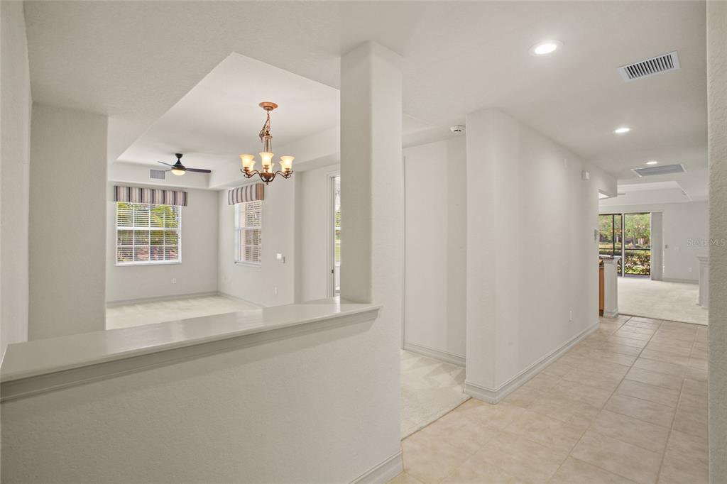 An interior view shows a tiled hallway leading toward a carpeted living area with a chandelier — 26207 AVENIDA LAS COLINAS, HOWEY IN THE HILLS, FL