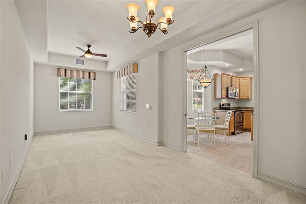 A carpeted room with a ceiling fan and chandelier leads into a kitchen with cabinets — 26207 AVENIDA LAS COLINAS, HOWEY IN THE HILLS, FL