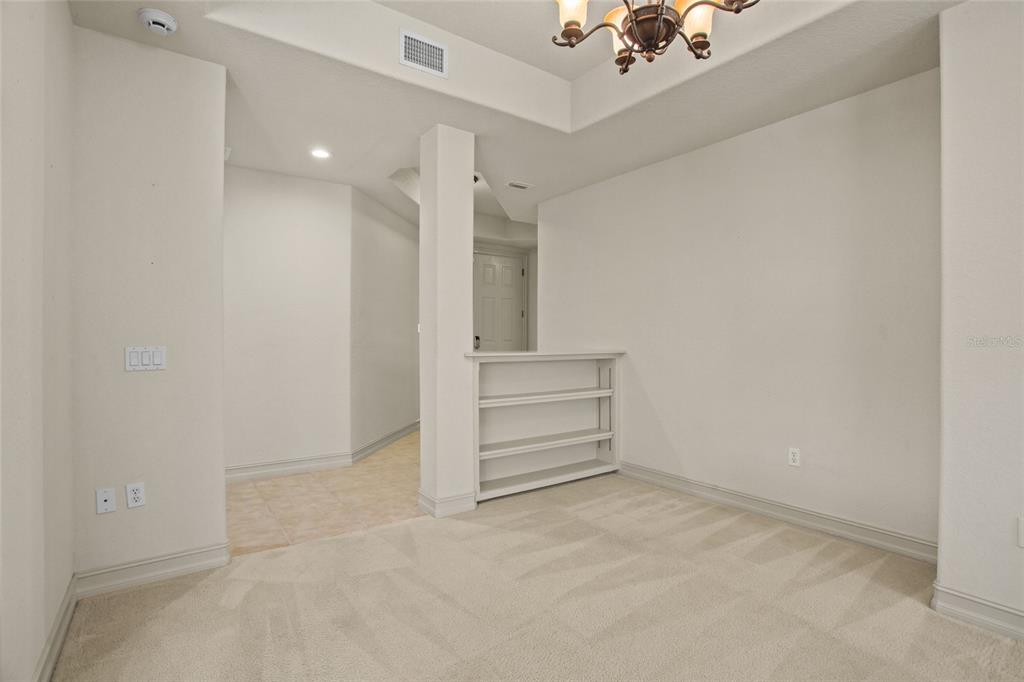An interior room features beige carpeting, a built-in bookshelf, and a tiled hallway entrance — 26207 AVENIDA LAS COLINAS, HOWEY IN THE HILLS, FL